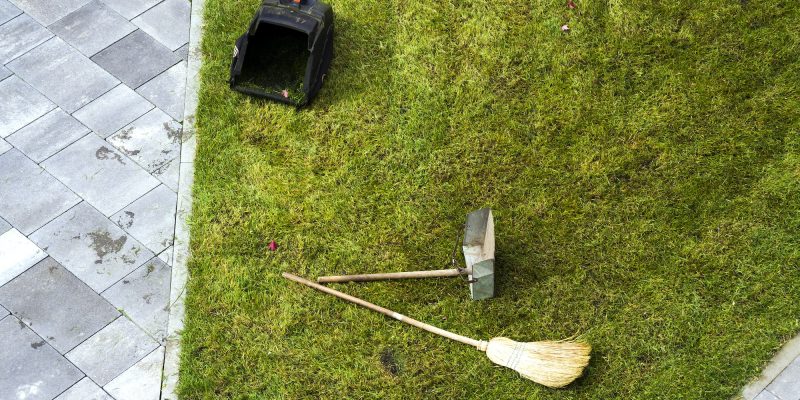 Jug dustpan and a broom on a green grass lawn. Gardening tools. Jug dustpan and a broom on a green grass lawn. Gardening tools.